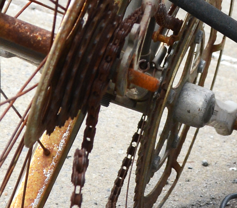 Abandoned broken and rusty bicycle chained to a metal pole on a pavement